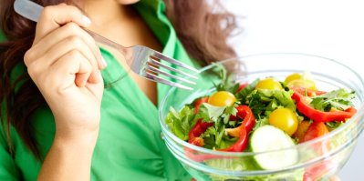 Žena drží misku se salátem, na vidličce má rajče