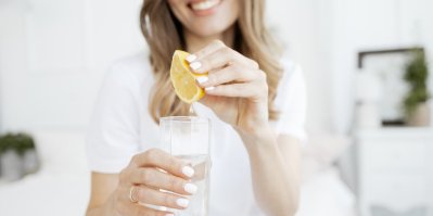 Žena vymačkává citronovou šťávu do sklenice s vodou