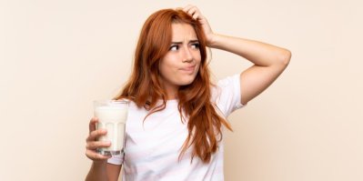 Žena drží sklenici s mlékem a tváří se zamyšleně