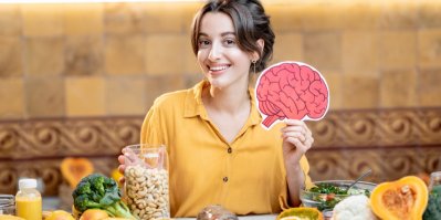 Žena držící model lidského mozku s různými zdravými čerstvými potravinami na stole