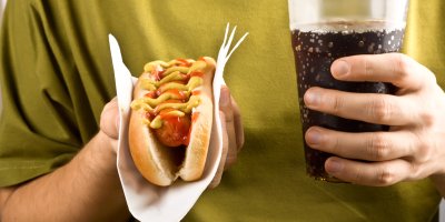 Člověk drží hotdog a kelímek s colou