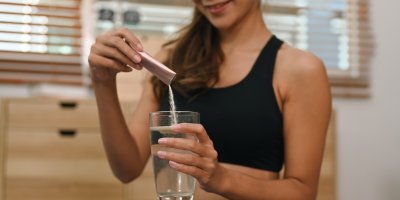 Žena si sype kolagenový doplněk ze sáčku do sklenice s vodou