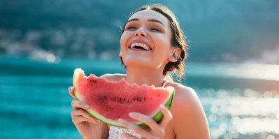 Smějící se mladá žena na pláži jí meloun