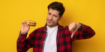 Muž drží hamburger a ukazuje palec dolů