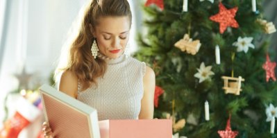 Žena se nespokojeně dívá na dárek, v pozadí vánoční stromek