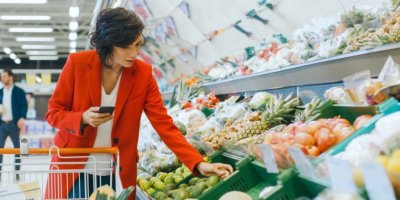 Žena nakupuje v supermarketu s mobilem v ruce