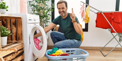 Muž se zdviženým prstem vyndává prádlo z pračky