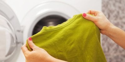 Žena, která drží v ruce žlutý svetr, vytažený z pračky