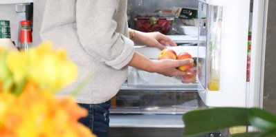 Postava drží v ruce ovoce před otevřenou ledničkou