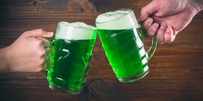 Dvě sklenice se zeleným pivem, které si k sobě ťukají
