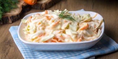 Salát Coleslaw, servírovaný v bílé míse, ozdobený snítkou kopru