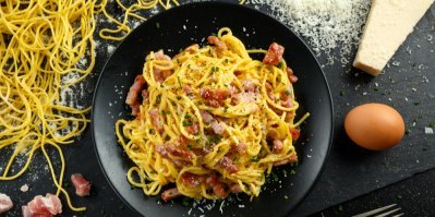 Špagety carbonara na černém talíři, kolem vejce, slanina a sýr