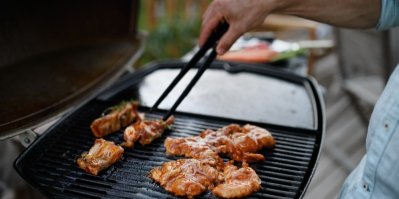 Muž obrací maso na venkovním grilu na rodinné zahradní slavnosti