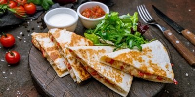 4 kousky quesadilly, servírované na dřevěném prkénku, se zeleninovou oblohou a 2 dipy