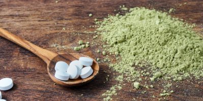 Bílé tabletky a dřevěné lžičce, okolo zelený prášek