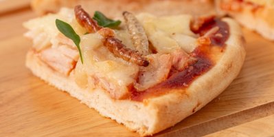 Hmyzí pizza, čerstvě upečená a krásně prezentovaná na dřevěném prkénku. Pizza je ozdobena lístky čerstvé bazalky