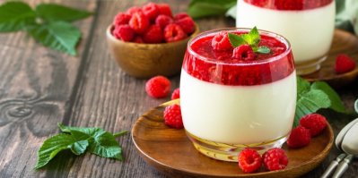 Panna cotta ve skleničce s malinovým přelivem, servírovaná na dezertním talířku s malinami