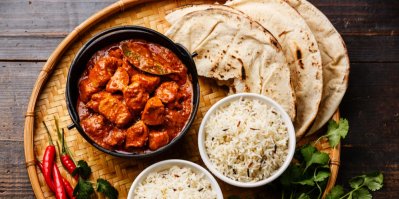 Kuřecí tikka masala v hnědé misce, vedle chléb naan a misky s rýží