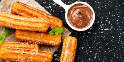 Několik churros, obalených v cukru, servírovaných na papíru. Vedle miska s čokoládovou omáčkou