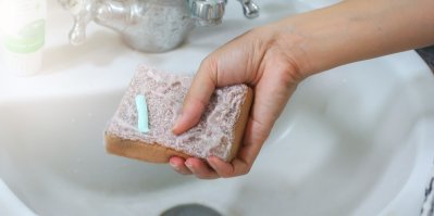 Houbička na mytí s nanesenou pastou v ruce nad umyvadlem
