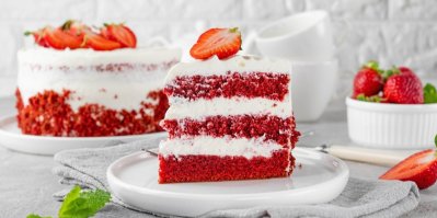 Ukrojený kousek dortu Red Velvet na bílém talíři, ozdobený rozkrojenou jahodou