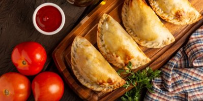 4 empanadas na dřevěném prkénku, vedle rajčata a rajčatový dip