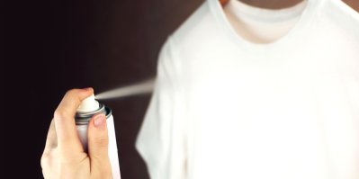Ženská ruka stříká sprej proti statické elektřině na bílé tričko