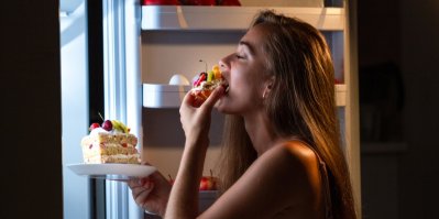 Mladá žena jí dezerty u otevřené lednice