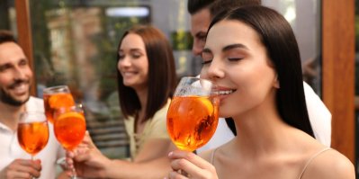 Žena pije Aperol Spritz, v pozadí jsou další lidé