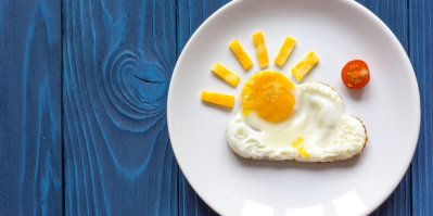 Talíř s osmaženým vejcem ve tvaru slunce a mraku, rozpůlené cherry rajčátko