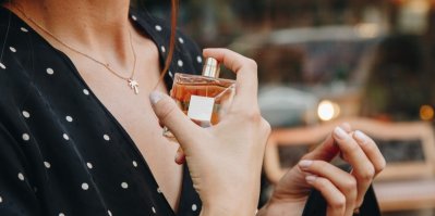 Žena si před zrcadlem stříká parfém na krk