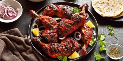 Kuře tandoori na hnědém talíři, kolem miska s kořením, indický chléb naan a miska s cibulí