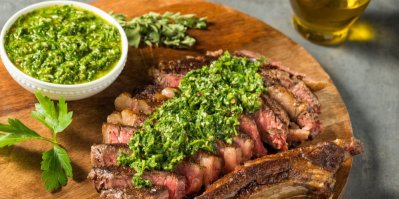 Nakrájený hovězí steak na dřevěném prkénku, přelitý chimichurri