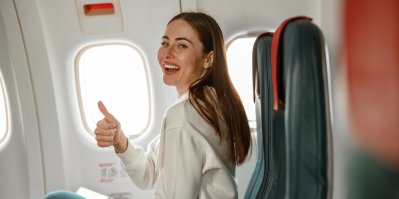 Mladá žena sedící v letadle ukazuje palec nahoru a usmívá se