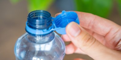 PET lahev s vodou, odšroubované neoddělitelné víčko drží člověk mezi prsty