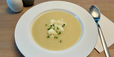 Květáková krémová polévka, servírovaná v bílém talíři