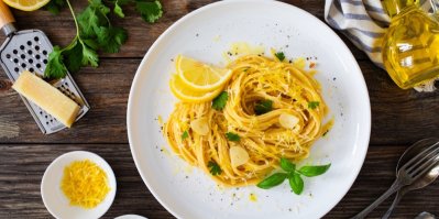 Talíř se špagetami a plátky citronu, vedle je struhadlo s kouskem sýra, olivový olej a vidlička se lžící