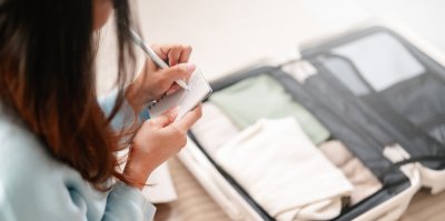 Žena si píše seznam u otevřeného kufru
