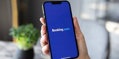 Ruka držící chytrý telefon s otevřenou aplikací Booking.com