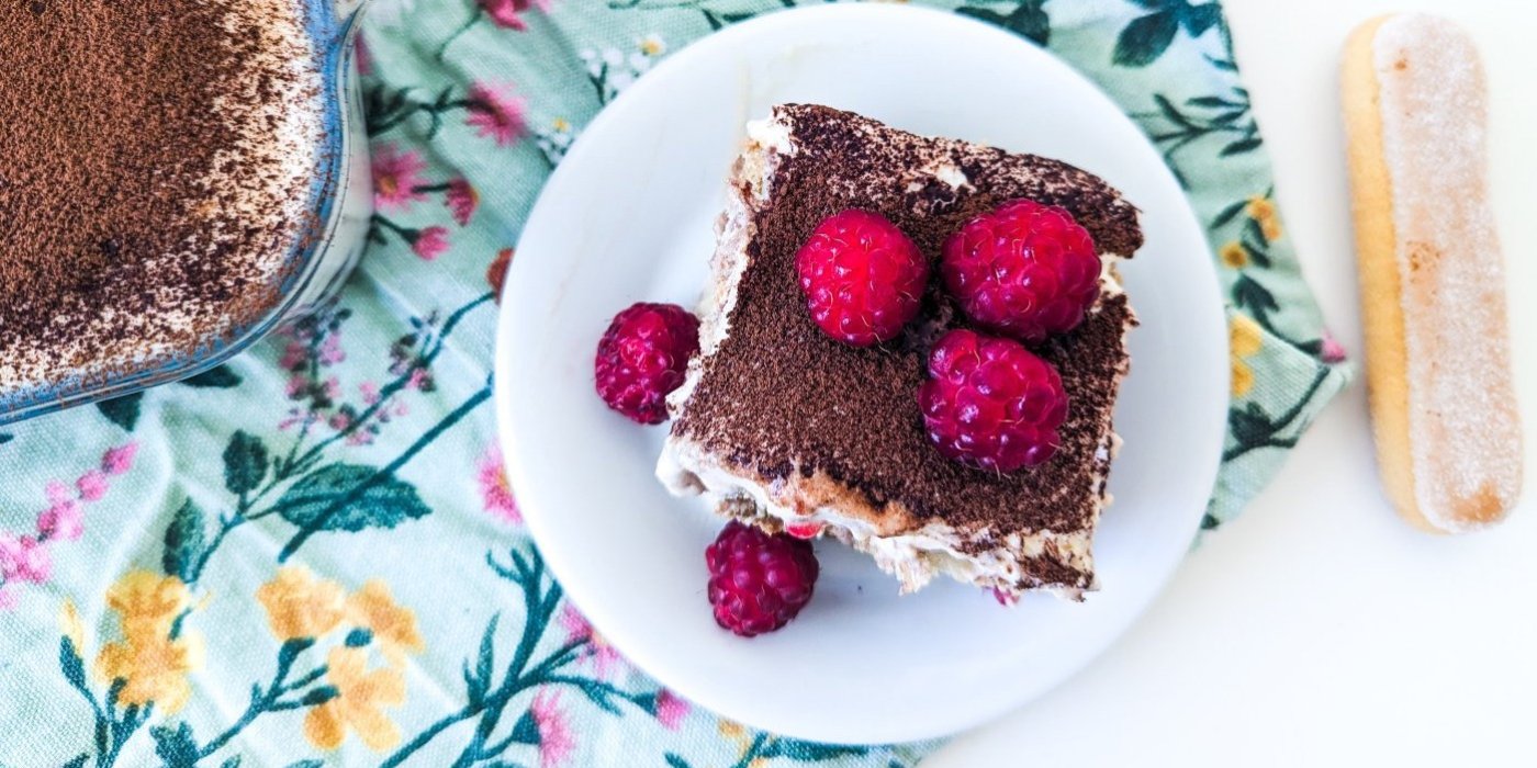 Kousek malinového tiramisu na bílém talíři, ozdobené malinami