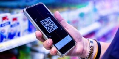 V obchodě stojí mladá žena drží v ruce chytrý telefon a skenuje QR kód na džusu