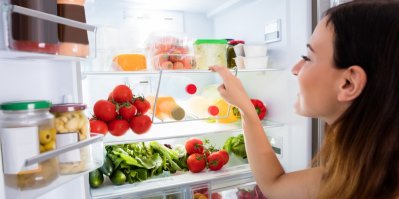 Žena se dívá do otevřené ledničky naplněné zeleninou a ovocem