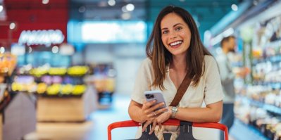 Mladá žena v supermarketu se usmívá a v rukou drží telefon.