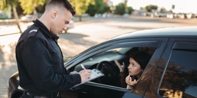 Žena sedí za volantem a policista sepisuje pokutu.