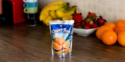 Nápoj Capri-Sun na stole, v pozadí ovoce