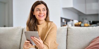 Žena sedí na pohovce s Apple tabletem v rukou.