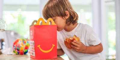 Dítě s hamburgerem v ruce se dívá do tašky McDonald's