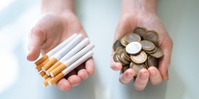 Člověk v jedné ruce drží cigarety a ve druhé euro mince