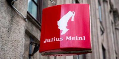 Detail staré budovy, na které je připevněn červený vývěsní štít s logem společnosti Julius Meinl