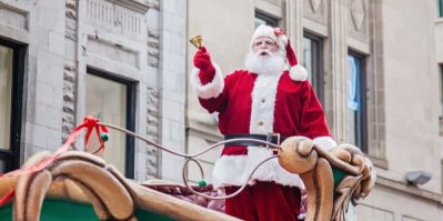 Muž v kostýmu Santa Clause stojí na saních a zvoní zvoncem.